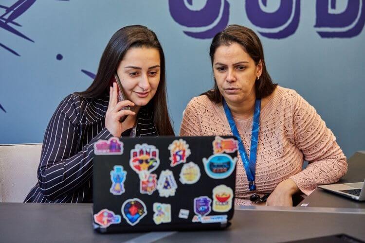 Women working together, talking on the phone, and looking at a computer.