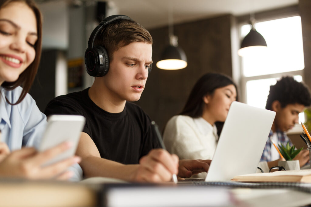 Grupo de estudantes estudando na biblioteca da universidade, foco em um cara sério olhando para o laptop
